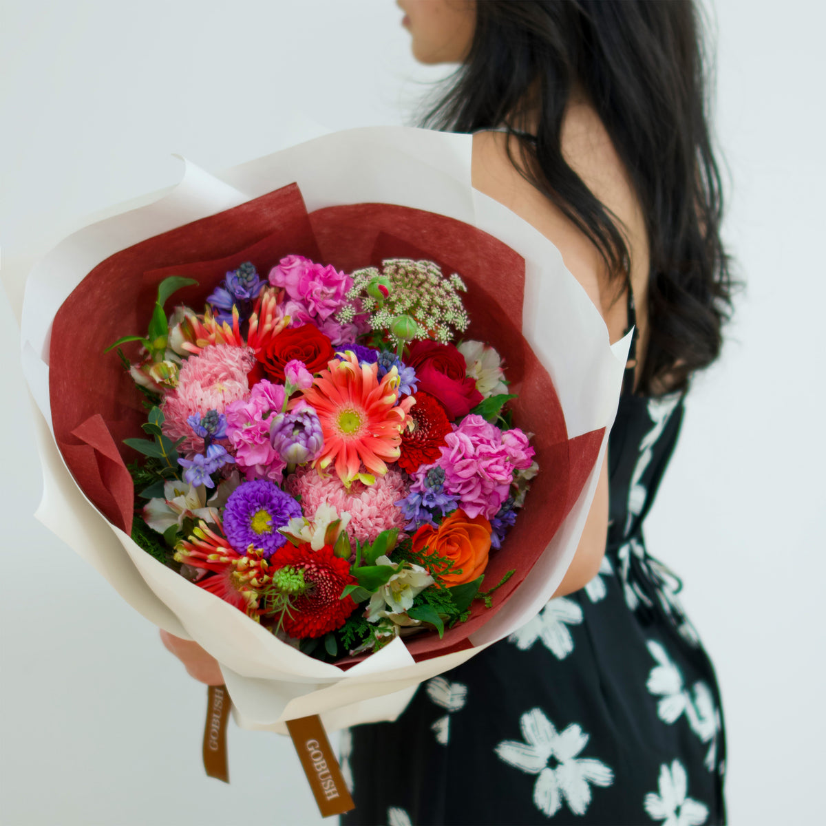 A vibrant, multicolored flower bouquet wrapped in white paper with a red interior liner. The bouquet features a variety of colorful flowers including pink, red, orange, purple, and green. designed by GoBush Florist Brisbane, in West end, Brisbane.