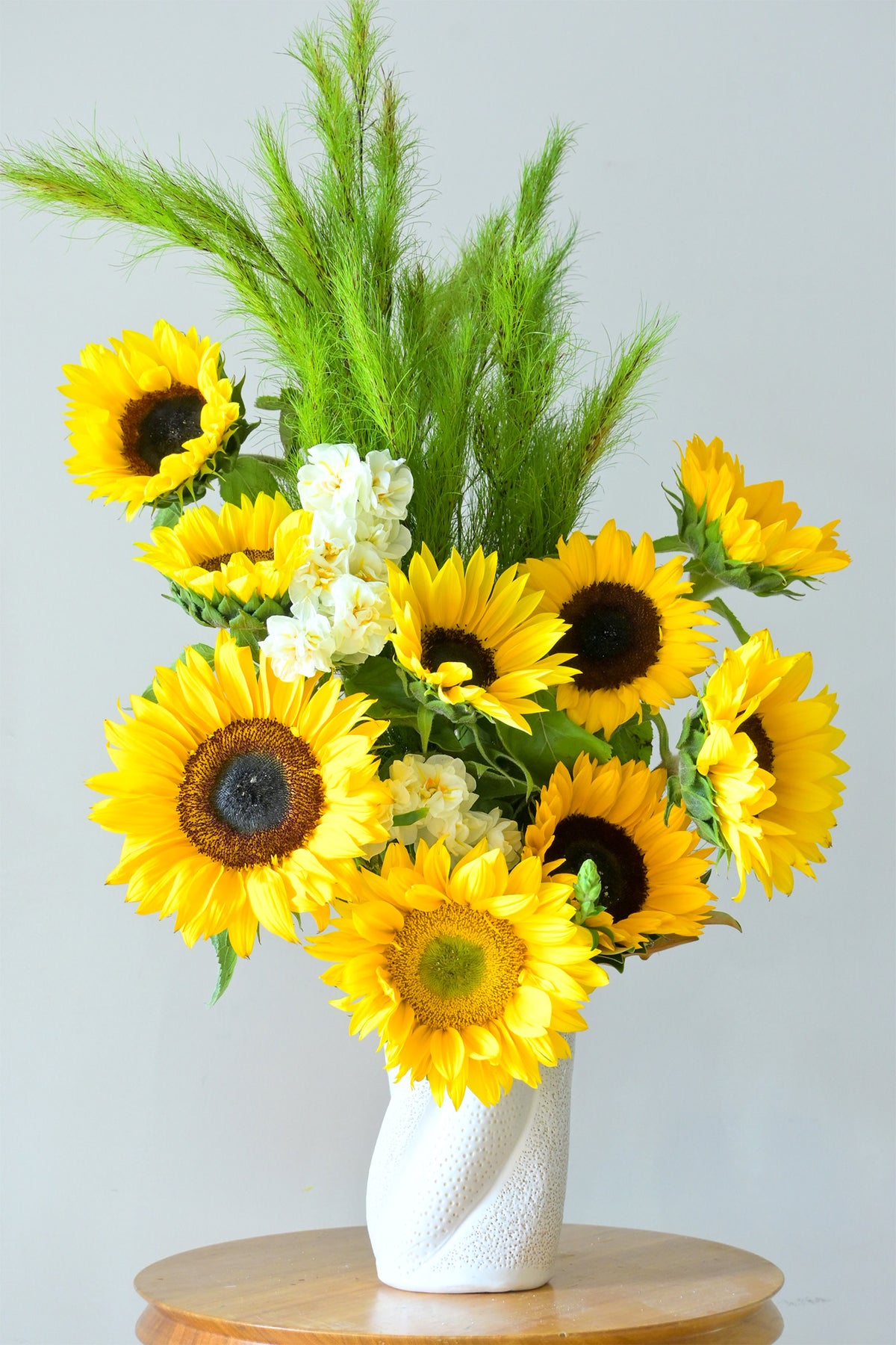 bright yellow sunflowers, green ornamental grass, and small white flowers in a textured white vase, GoBush florist Brisbane. 