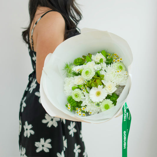 green and white flower bouquet wrapped in white paper with a green ribbon. The bouquet features white daisies, white roses, and green foliage. designed by GoBush Florist Brisbane, in West end, Brisbane.
